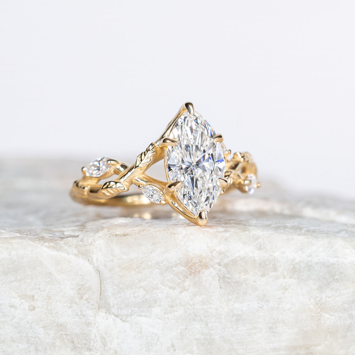 Gold leaf and vine split shank ring with a diamond on a light marble surface