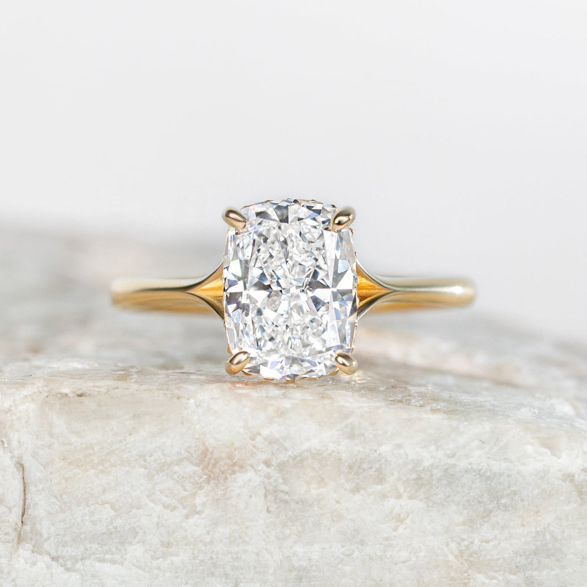 Yellow Gold elongated cushion solitaire engagement ring on white marble background