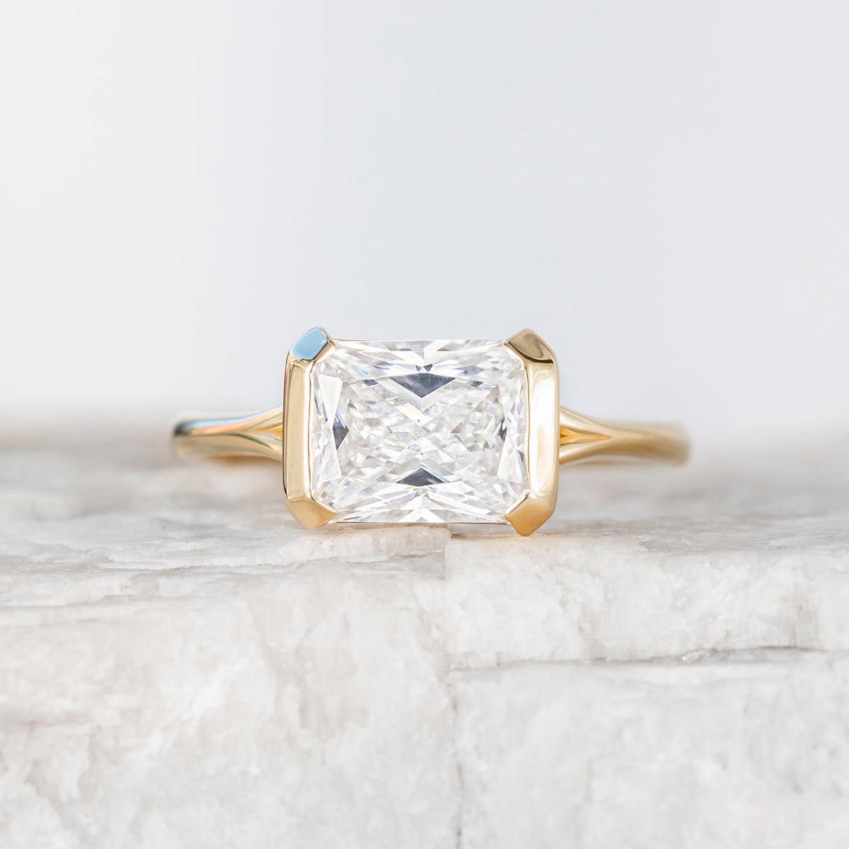 A ring with a half bezel setting featuring a central diamond, with a hidden diamond halo on the sides, crafted in yellow gold.