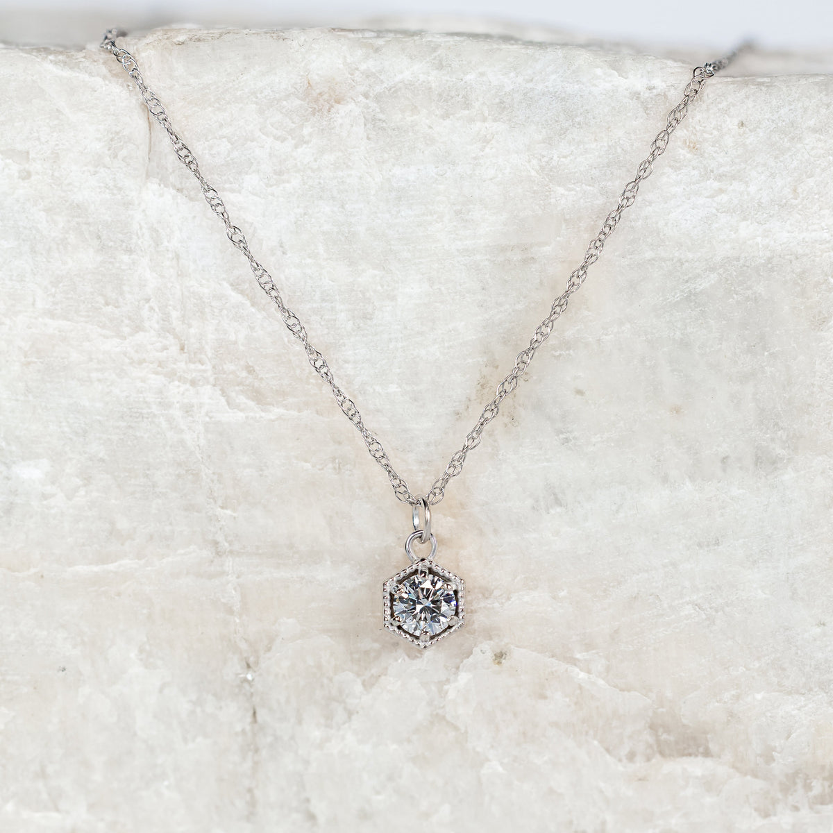Hexagonal necklace with a diamond pendant on a textured white surface