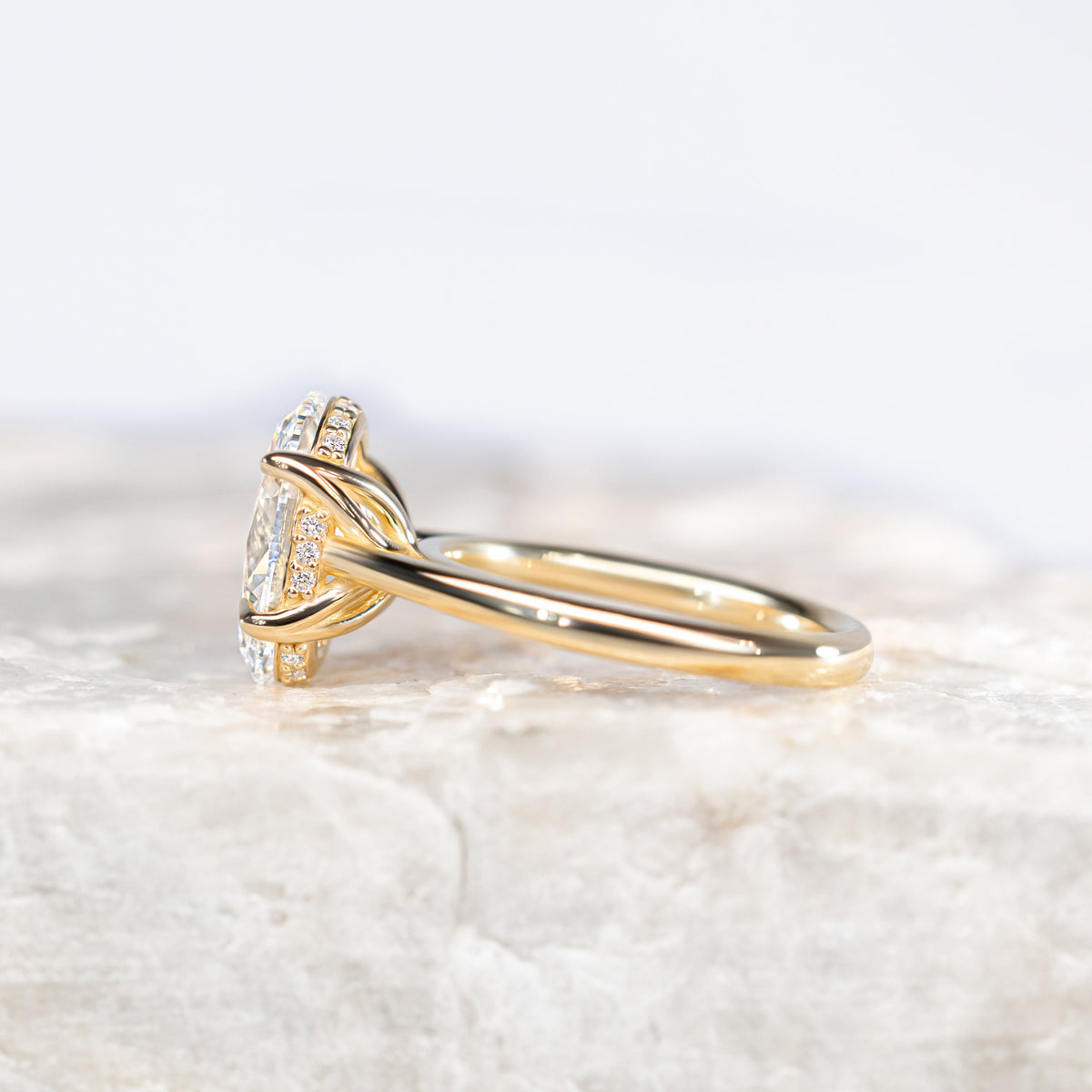 Oval Diamond Solitaire Petal Prong Engagement Ring in Yellow Gold sitting on a white marble surface