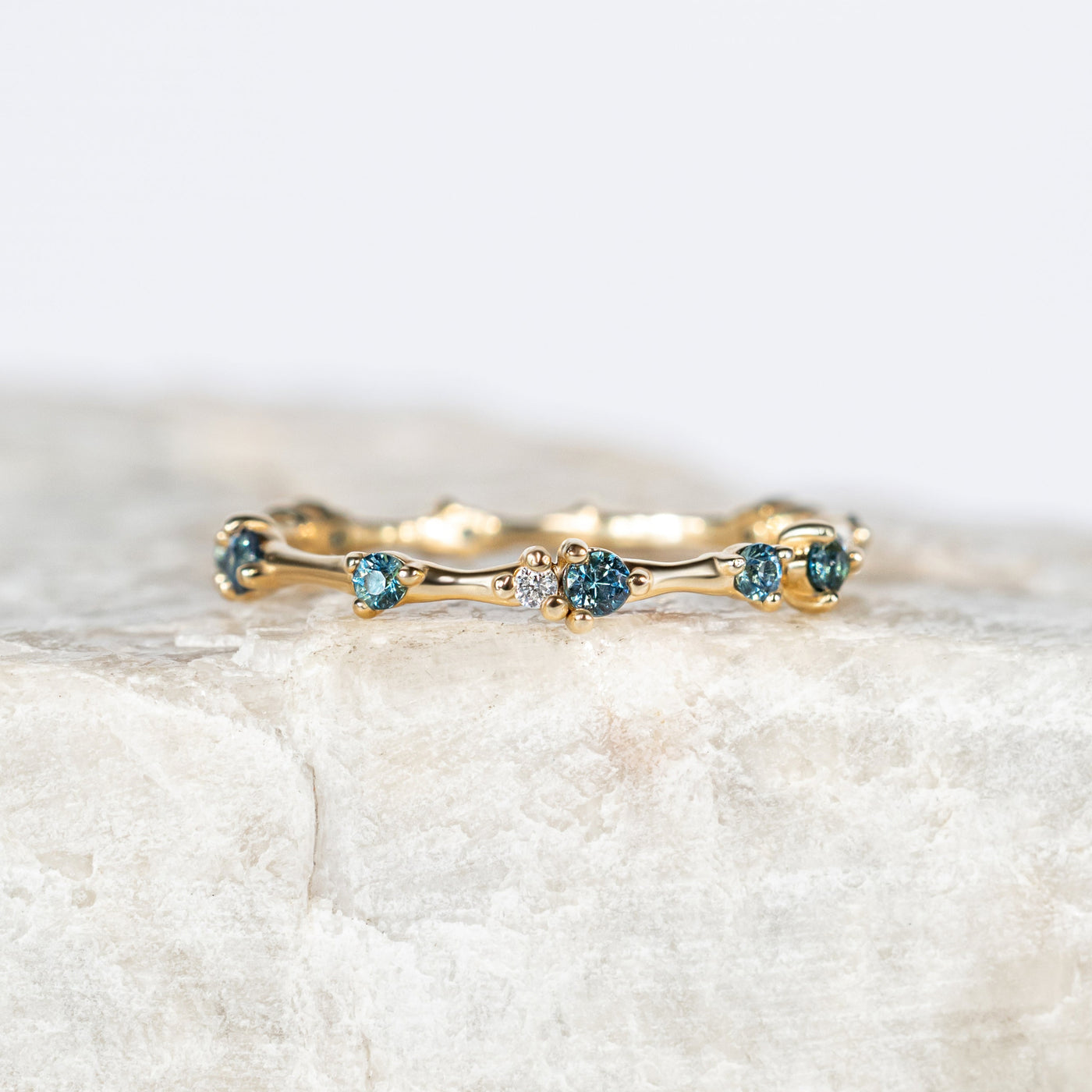 Gold organic ring with small blue sapphires on a light marble background