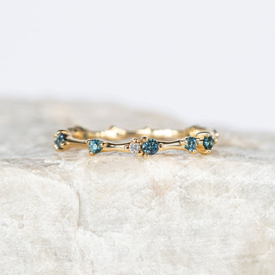 Gold organic ring with small blue sapphires on a light marble background