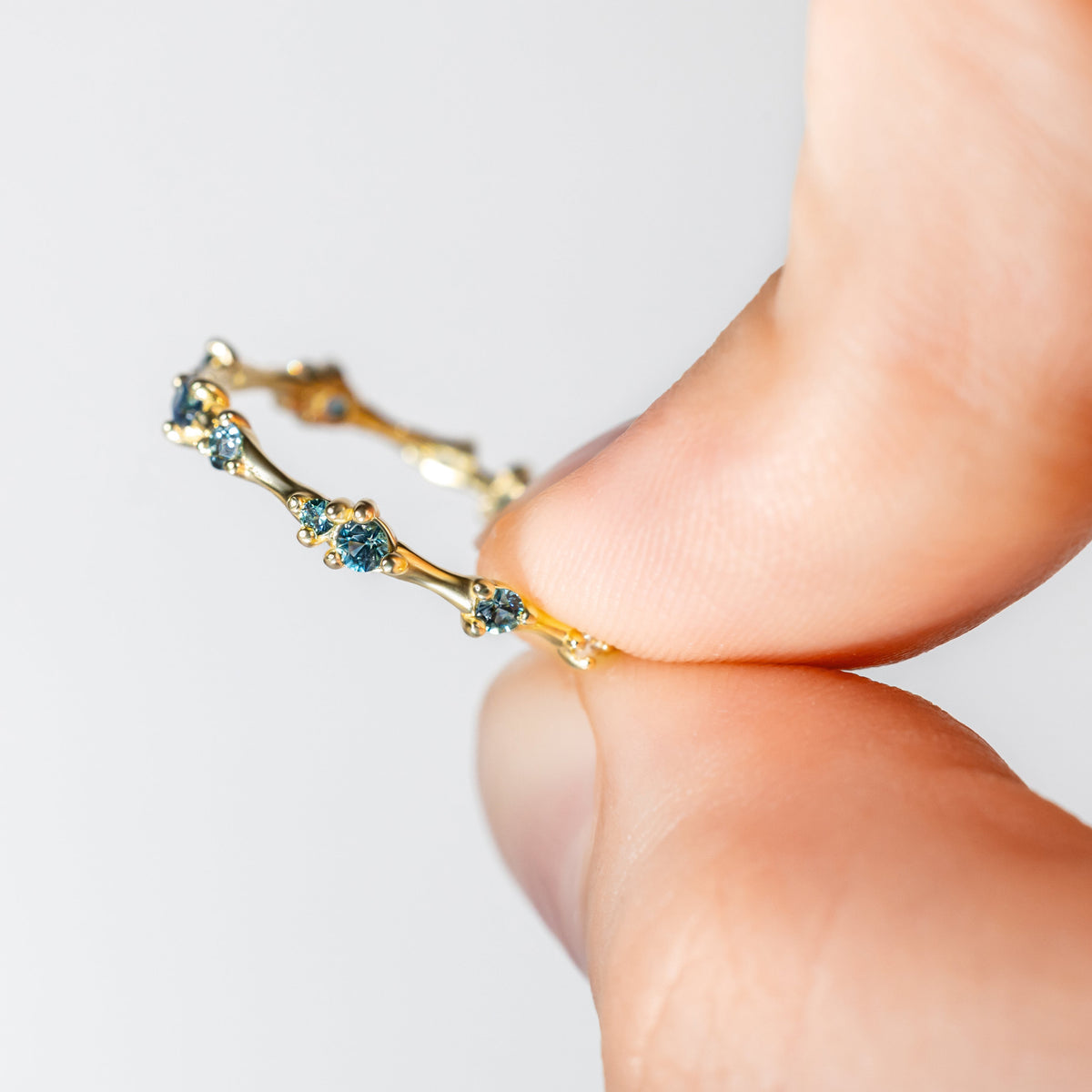 Gold ring with blue sapphires pinched by fingers