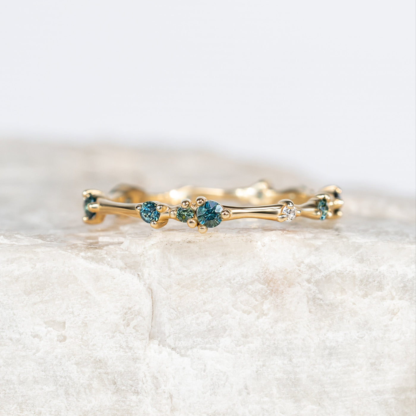 Gold organic ring with small blue sapphires on a light marble background