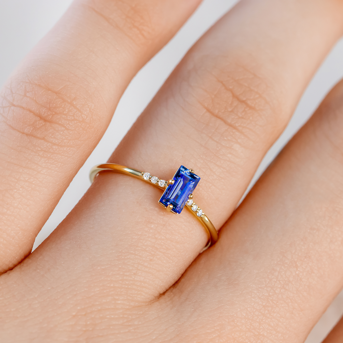 Gold ring with a blue gemstone on a finger against a neutral background