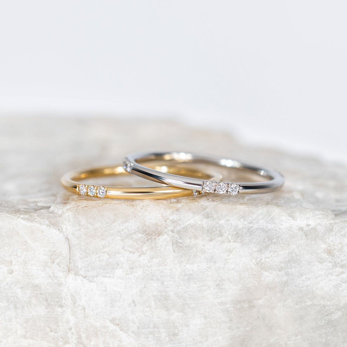 Two gold rings with diamonds on a textured white surface