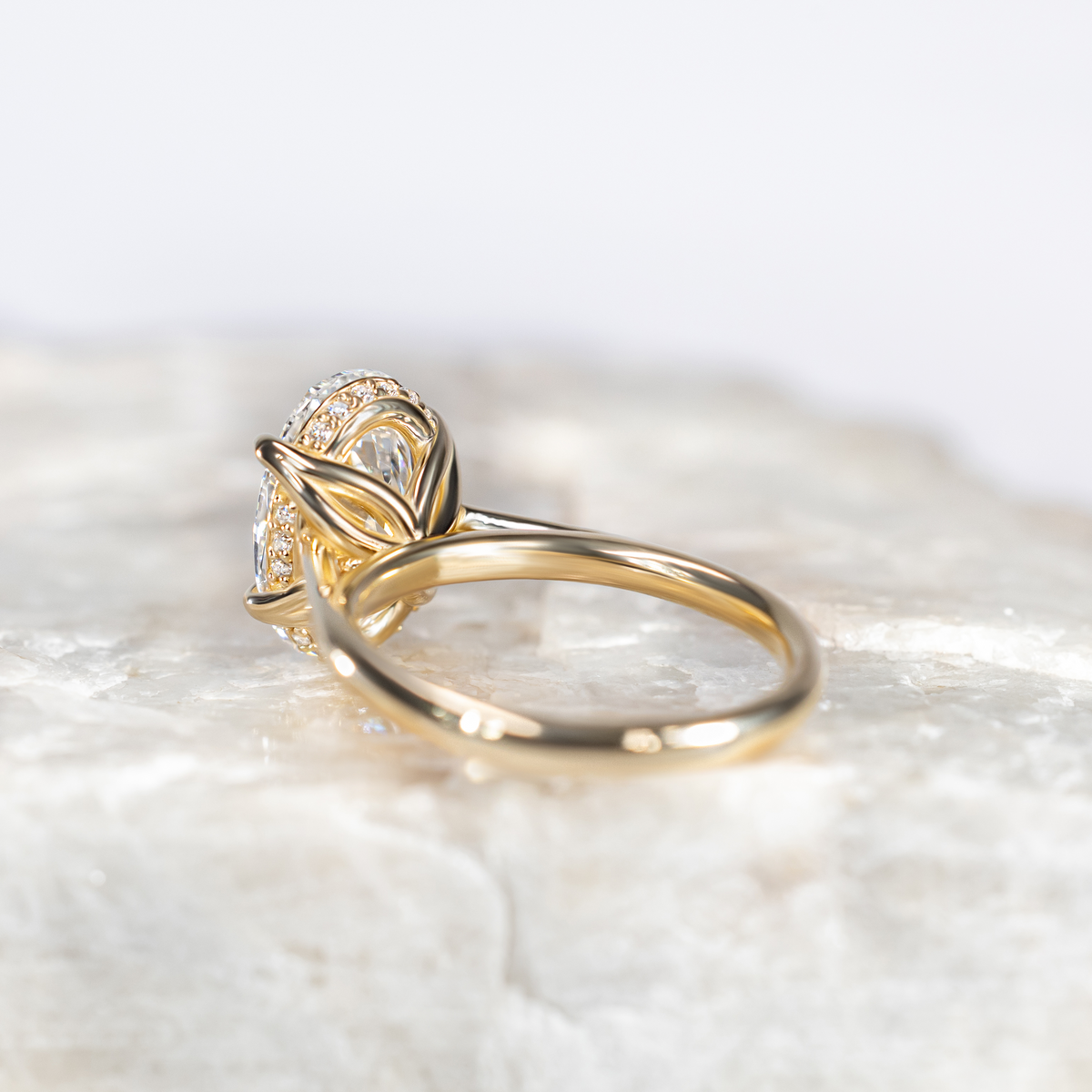 Oval Diamond Solitaire Petal Prong Engagement Ring in Yellow Gold sitting on a white marble surface