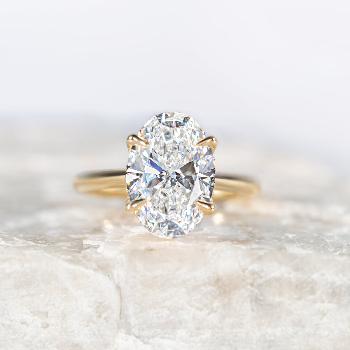 Oval Diamond Solitaire Petal Prong Engagement Ring in Yellow Gold sitting on a white marble surface